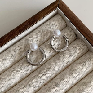 Close-up of C-shaped silver pearl earrings displayed in a luxury velvet jewelry box