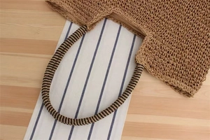 Close-up of handwoven straw bag featuring striped crossbody strap and fabric lining detail