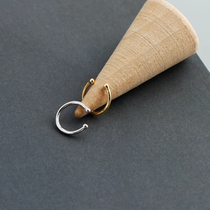 Minimalist C-shaped silver and gold ear cuffs displayed on a small wooden cone stand