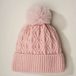 Pink chunky knit beanie with large faux fur pompom and diamond texture on beige background