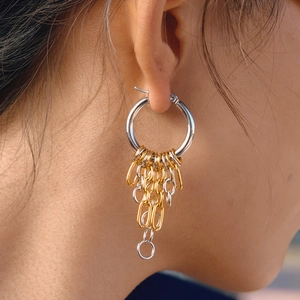 Macro view of two-tone stainless steel hoop earrings with layered tassel chains on a model