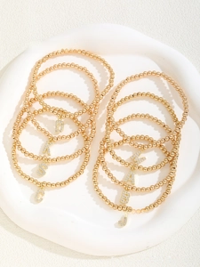 Close-up of gold beaded elastic bracelets with crystal-encrusted letter pendants on white tray