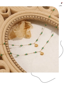 Detail of gold shell pendants and green crystal beads on a thin chain necklace