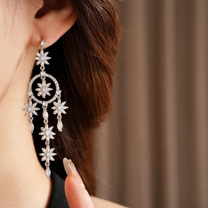Close-up of silver tassel earrings with zircon flowers worn by a model in soft lighting