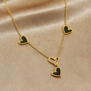 Collana dorata con pendenti a cuore neri e cavi su sfondo di raso champagne