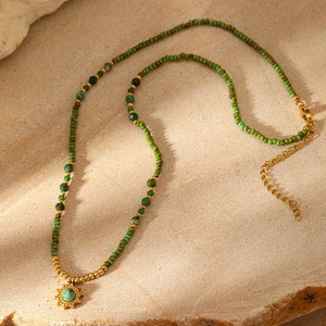 Detail of green beaded necklace with gold sun flower pendant on stone surface