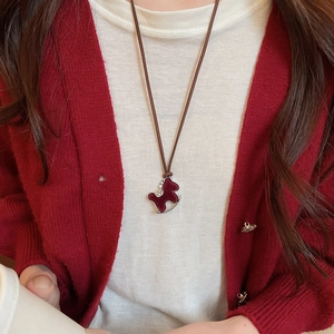 Close-up of a burgundy pony pendant necklace with zircon inlay on a red cardigan