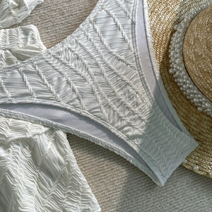 Detail eines weißen Bikinisets mit V-Muster-Strukturstoff und Perlenstrohhut