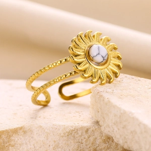 Detailed shot of golden sunburst ring with round white stone on beige stone base