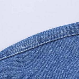 Nahaufnahme von blauem Denim-Stoff mit Faserstruktur und gelben Kontrastnähten im Detail