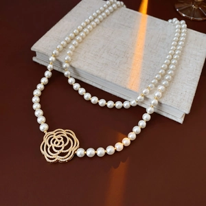 Detail of double-layer pearl necklace with a gold camellia pendant on a dark surface