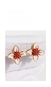 Macro detail of white enamel flower earrings with red accents and gold core detailing