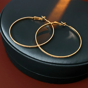 Close-up of large gold-plated hoop earrings on a black leather jewelry box lid