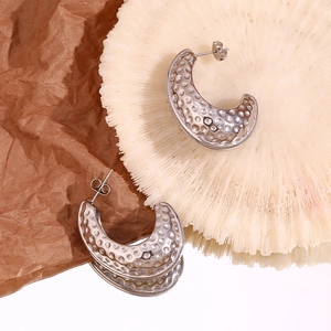 Détail des boucles d'oreilles argentées en C avec texture martelée sur fond créatif