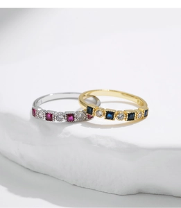 Detailed view of silver and gold rings with square colored stones on white stone base