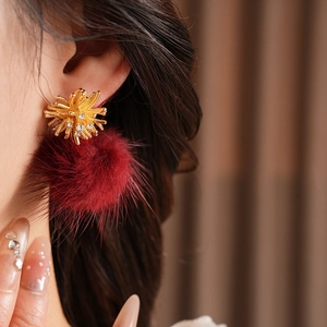 Detail of elegant fireworks gold stud earring with a dark red plush pompom on a model