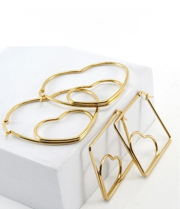 Polished 18K gold heart-shaped and geometric hoop earrings on minimalist display