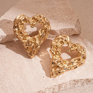 Macro detail of gold hollow heart earrings with vintage molten texture on a stone background