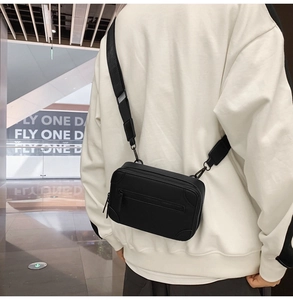 Rear view of model wearing a black matte rectangular crossbody bag with wide strap