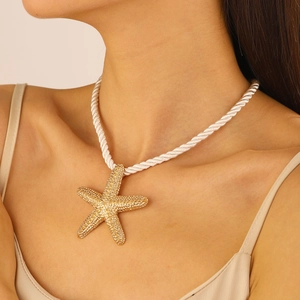 Detailed view of model wearing a large golden starfish pendant with white braided cord necklace
