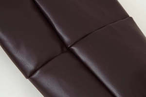 Macro shot of dark brown quilted faux leather texture with padded double-breasted jacket detail