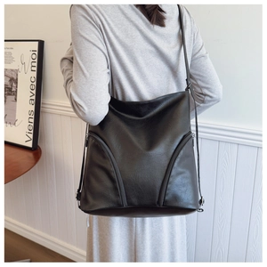 Detail of black PU leather shoulder bag featuring dual curved zippers and soft texture