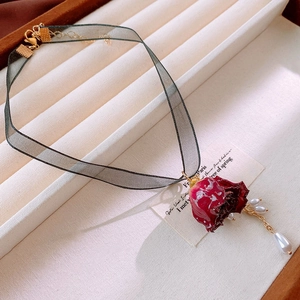 Close-up of deep green lace choker with red rose pendant and pearl tassels on velvet