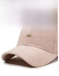 Detail of light pink herringbone wool baseball cap featuring a gold ollo metal logo