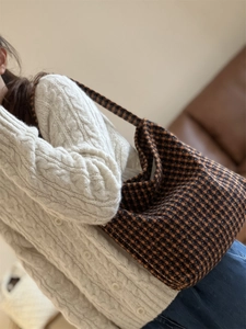 Close-up of a vintage plaid woolen hobo bag worn by a model in a cozy indoor setting