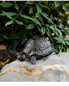 Detailed close-up of a vintage cast iron turtle key box on a natural rock with garden background