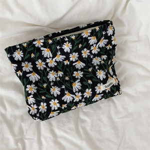 Close-up of white daisy embroidery on a black cotton makeup bag with brand label