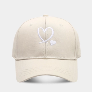 Detailed view of heart embroidery on cream cotton baseball cap with curved brim