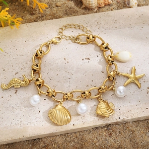 Bracelet doré aux breloques marines avec hippocampe et perle sur fond de plage