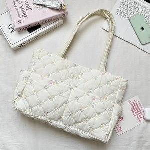 Macro detail of white quilted tote bag featuring floral embroidery and front slip pocket