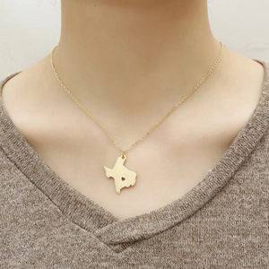 Golden Texas state map necklace with heart cutout worn on a brown knit sweater