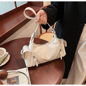 Detail of creamy white glossy leather shoulder bag with multi-zipper design and straps