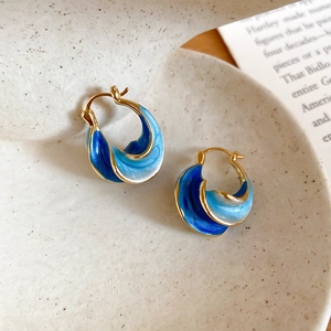 Detailed close-up of blue gradient enamel earrings with gold trim on a ceramic dish