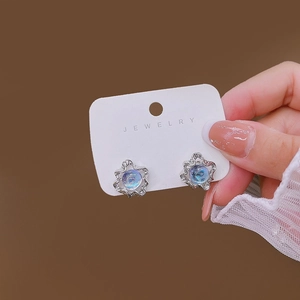 Close-up of irregular silver floral stud earrings with blue opal stones held by hand