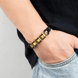Close-up of men's gold stainless steel chain and black braided leather bracelet on wrist