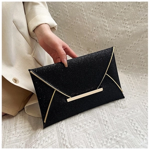 Détail d'une pochette de soirée à paillettes noires avec barre dorée tenue à la main