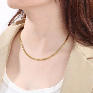 Gros plan d'un collier chaîne Figaro doré porté sur un blazer beige de style élégant