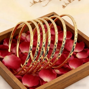 Detail of seven gold-colored stacked diamond-cut bangles in a wooden box with red roses