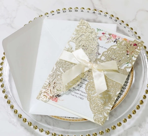 Detailed laser-cut gold wedding invitation with floral insert and cream ribbon bow