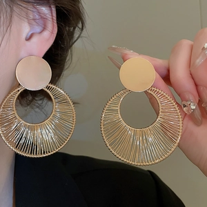 Detailed view of large golden woven metal hoop earrings with intricate wire wrapping
