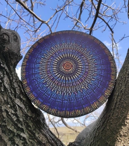 Detailed view of colorful mosaic drum with mandala pattern held against a clear blue sky