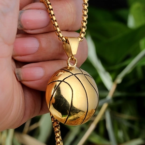 Close-up of a gold basketball pendant necklace on a steel box chain held by hand