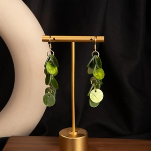 Detail of layered green resin disc drop earrings with gold hooks on black display