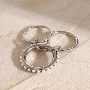 Close-up of interlocking silver stainless steel rings with white pearls on stone