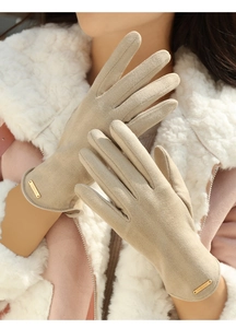 Detailed close-up of beige suede-feel gloves featuring a metal Fashion badge on the cuff