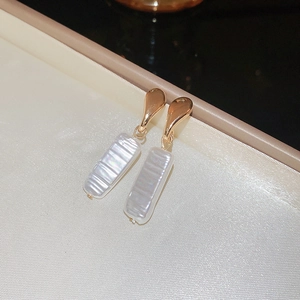 Detailed view of elegant gold drop earrings with textured white shell pendants on silk